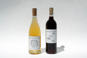 Two bottles from Broc Cellars Amore Duo stand side by side against a plain background. Amore Bianco, an Italian table wine, is on the left with a floral label. On the right is Amore Rosso, showcasing similar floral artistry and sourced from renowned Fox Hill Vineyard.