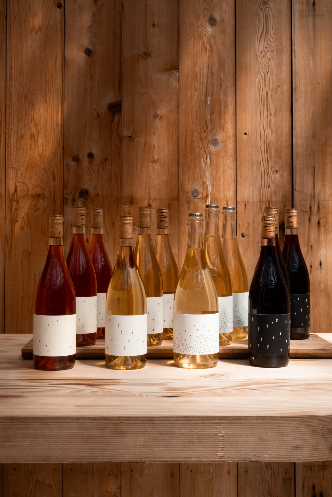 A selection of Broc Cellars’ Love Case wines—red, white, rosé, and a special Love Rosé with blank white labels and gold caps—are displayed on a wooden table against a wood-paneled wall.