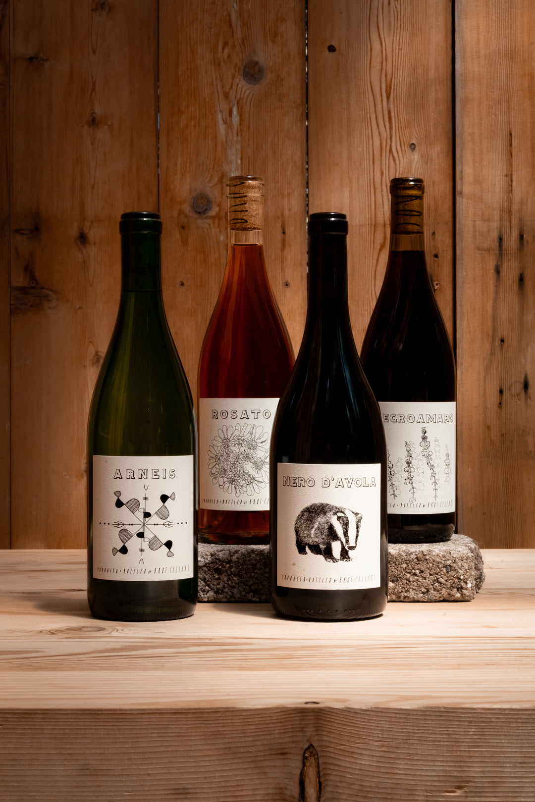 Four Fox Hill 4-Pack wines by Broc Cellars—Arneis, Rosato, Nero D’Avola, and Mezzodanno—are shown with illustrated white labels on a wooden surface; two bottles rest on stone blocks.