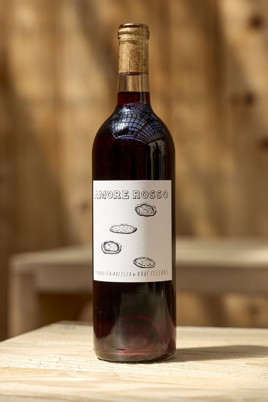A bottle of 2023 Amore Rosso Italian red table wine with a label featuring the text Amore Rosso above illustrations of three small, oval shapes.