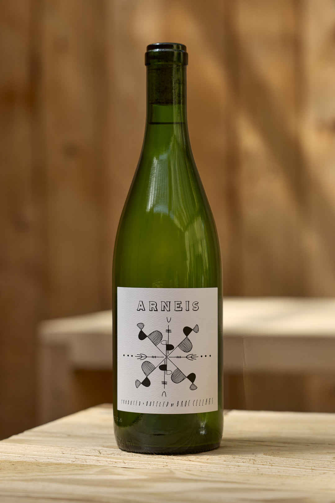 A bottle of Broc Cellars 2024 Arneis white wine with a white label featuring the text Arneis above a geometric line art design.