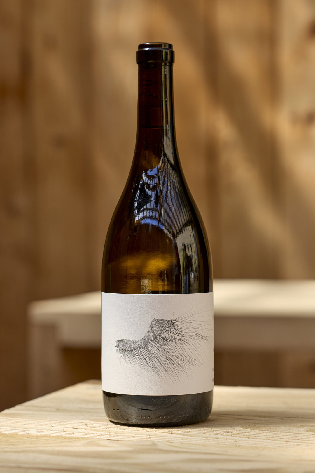 A bottle of 2023 Michael Mara Chardonnay with a white label featuring a black and white line drawing of a stylized eyelash or feather.