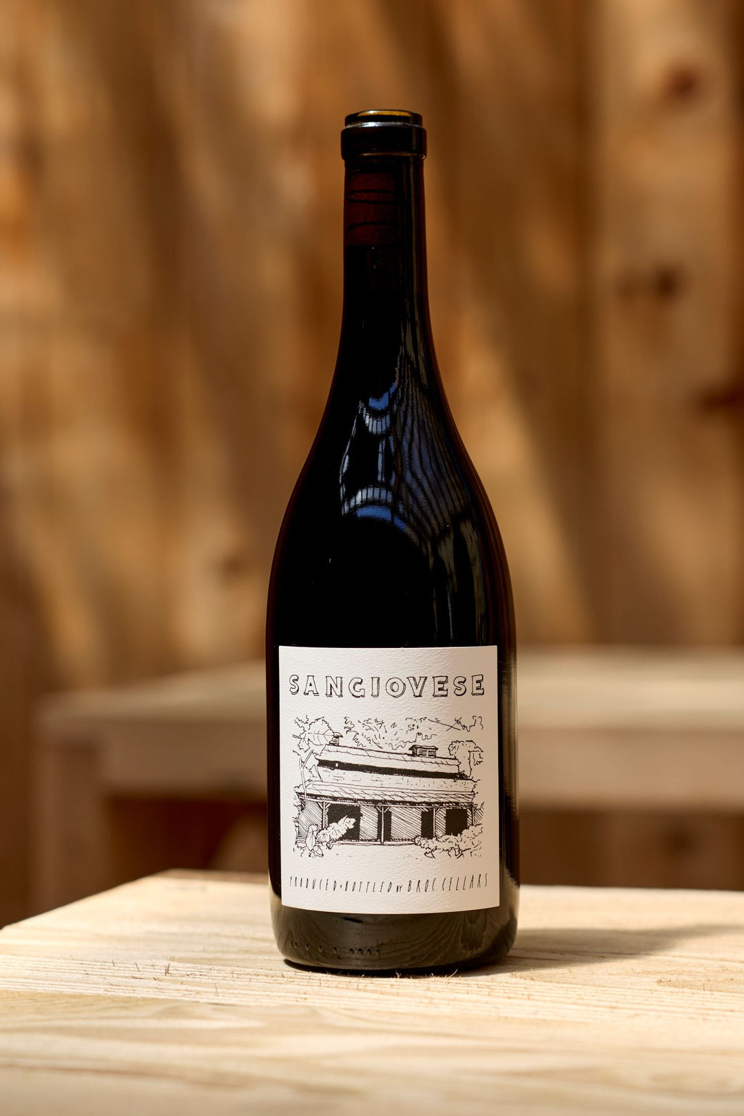 A bottle of Broc Cellars 2025 Sangiovese red wine with a white label featuring an illustration of a house and gentle tannins.