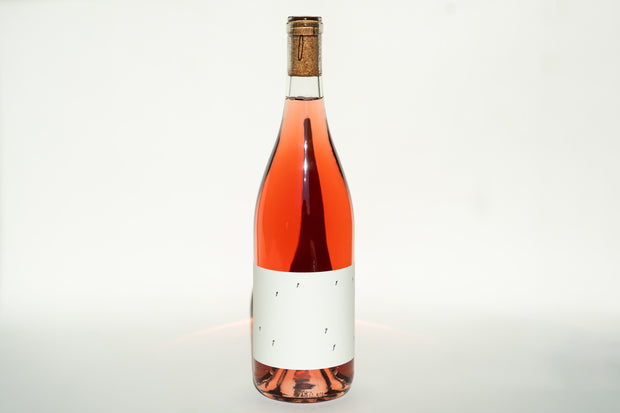 A bottle of 2024 Love Rosé by Broc Cellars, featuring a cork stopper, is set against a plain white background. It has a minimalistic white label with delicate black markings that highlight the wines light pink hue.