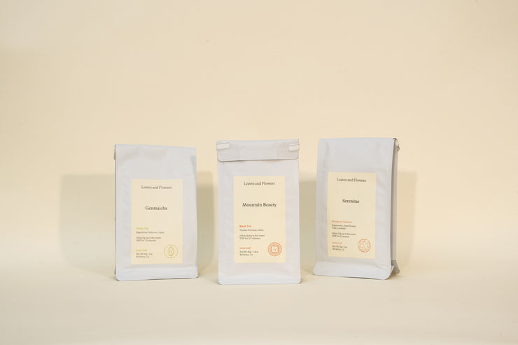 Three white bags labeled “Genmaicha,” “Mountain Beauty,” and “Sencha” from Broc Cellars’ Mothers Day Packs stand side by side against a neutral background, each featuring minimalist labels with additional text beneath the names.