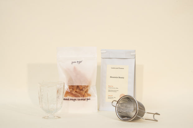 The Broc Cellars Mothers Day Packs include a clear glass, a white pouch of dried moss candied peel, a Mountain Beauty tea bag, and a metal tea infuser arranged on a light background.