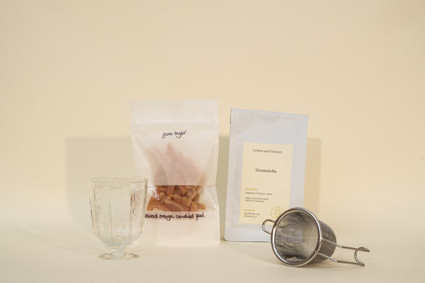 The Broc Cellars Mothers Day Packs features a clear glass, brown rock sugar, a Genmaicha tea packet, and a metal infuser arranged on a light surface.