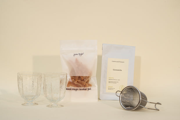 The Broc Cellars Mothers Day Packs includes two clear glass cups, a bag of brown rock sugar, a Lemons and Flowers Genmaicha tea packet, and a metal tea strainer—all set against a light background.