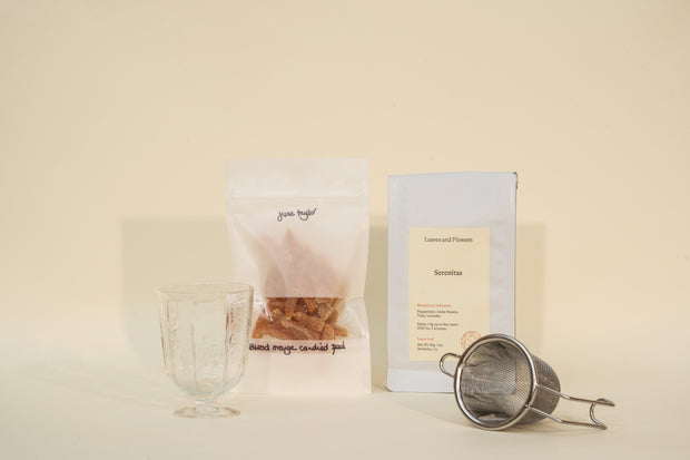 Broc Cellars Mothers Day Packs featuring a clear glass, metal tea strainer, white Senritsu tea bag, and transparent Blend Magic candied peel pouch are arranged on a neutral background.
