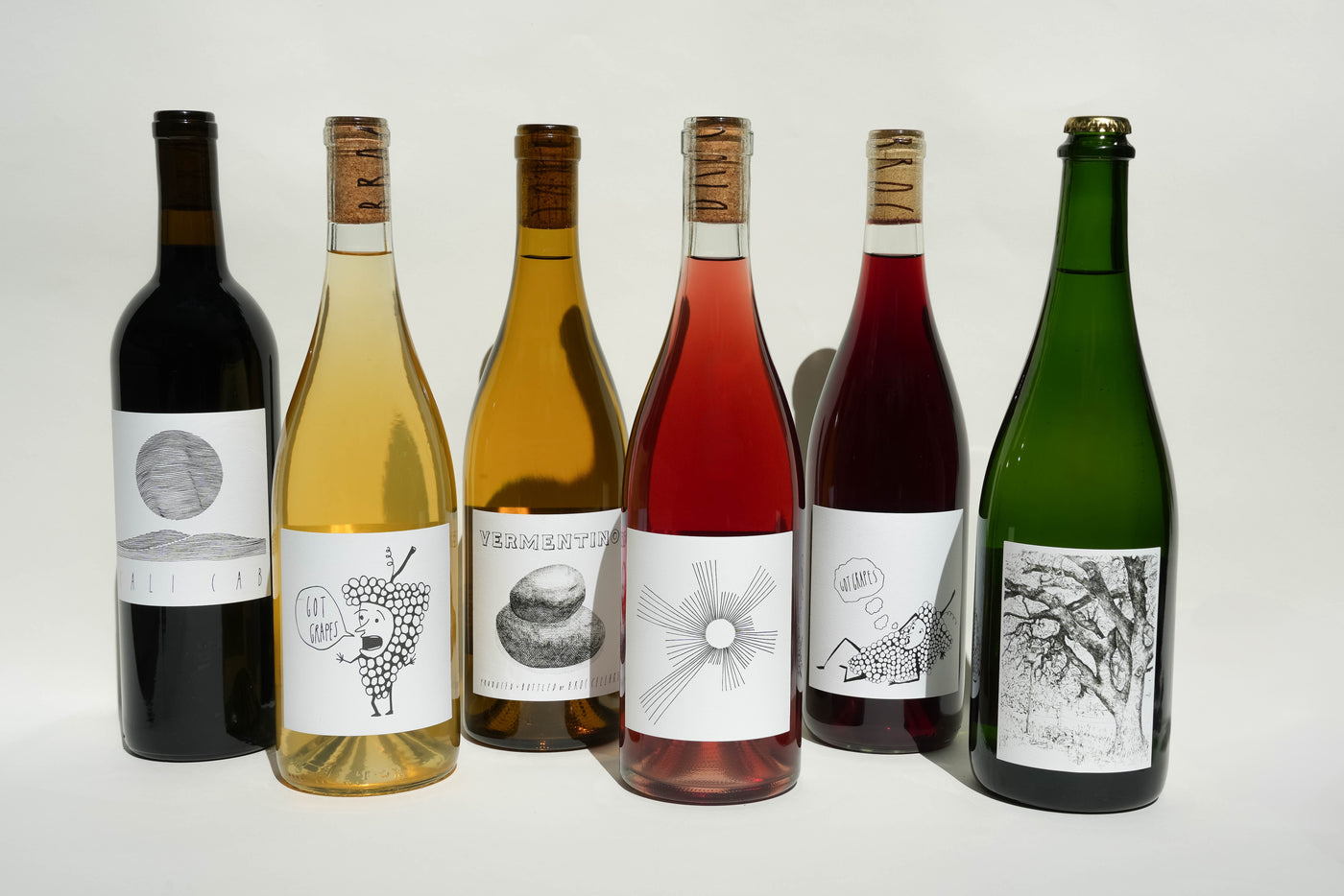 Six bottles of Broc Cellars 2025 Summer Club Classic stand against a white background, each displaying distinct shapes, wine hues, and minimalist black-and-white labels with abstract or nature-themed illustrations.