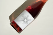 A glass bottle of 2024 Oh Sunshine rosé by Broc Cellars, featuring a modern white label with minimalist black lines radiating from a central circle, rests on a light surface casting a shadow.