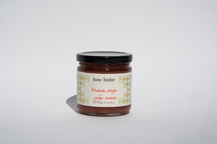 A jar with a black lid, labeled Broc Cellars, contains June Taylor Rhubarb, Orange & Ginger conserve, made from hand-cut fruit. The product supports sustainable agriculture and is elegantly displayed on a plain white background.