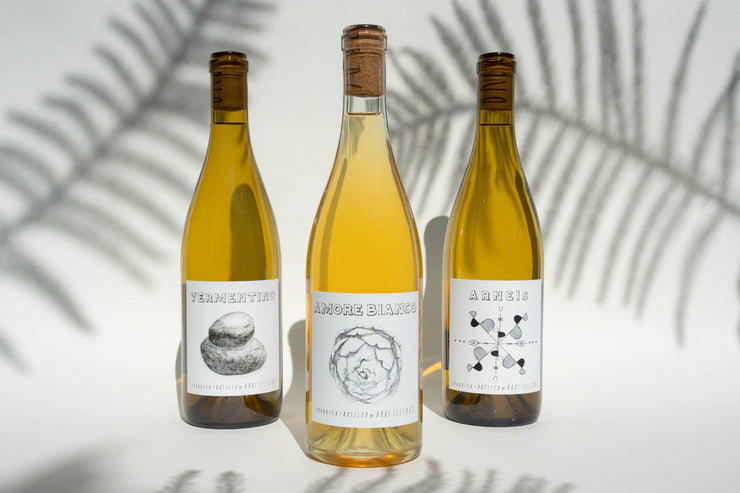 Three bottles of Fox Hill Whites by Broc Cellars sit against a light backdrop with shadows. Each bottle presents its own label design, showcasing the names Vermentino, Amore Bianco, and Arneis, adorned with artistic illustrations.