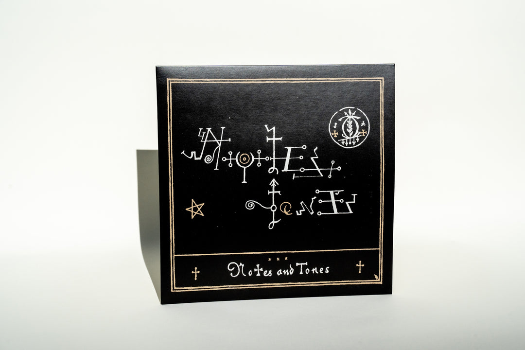 The Notes &amp; Tones V.2 - The Album from Broc Cellars features a black cover with an intricate gold design of abstract symbols and lines, evoking a DJ Muggs album. Its star and geometric shapes stand out against the plain background, inviting readers into its collaborative world.