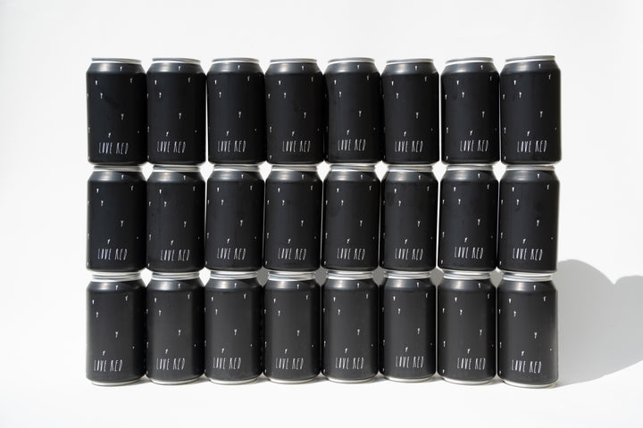Twenty Broc Cellars Love Red Can Packs with black labels, arranged in four rows on a white background; each can displays “LOVE RED” in bold white letters and features California red wine crafted from old heritage vines.
