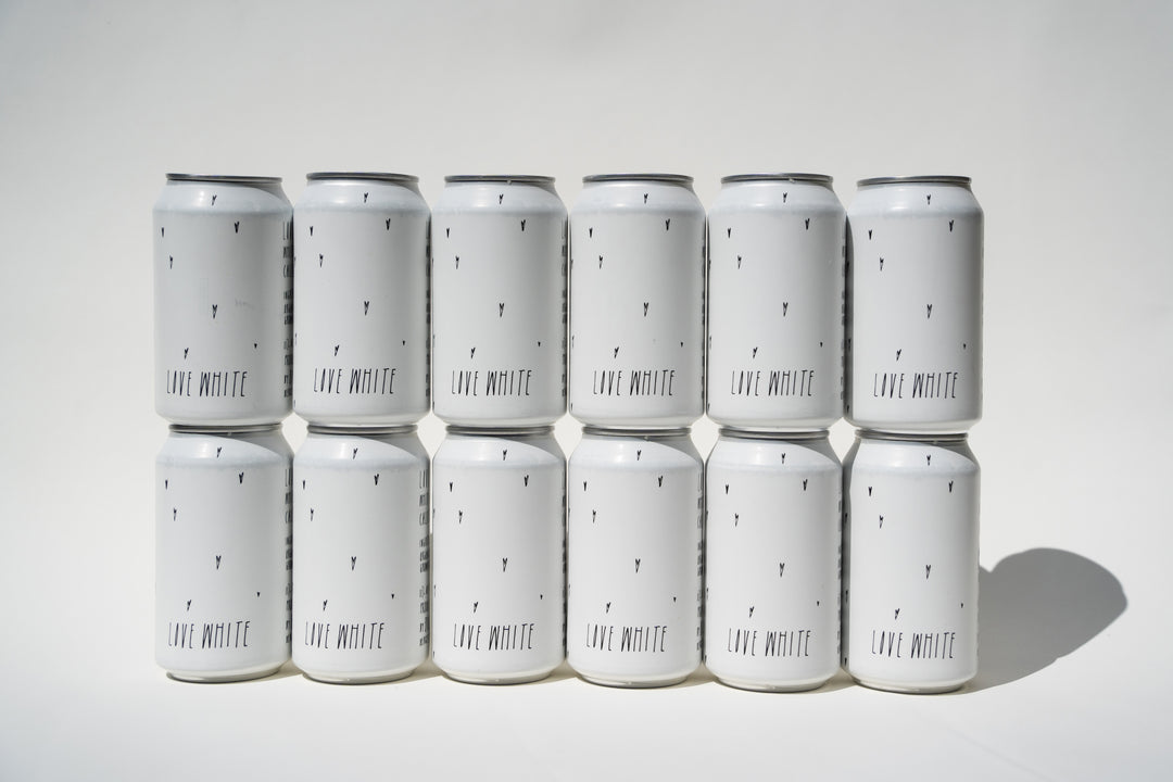 Twelve Love White Can Pack cans by Broc Cellars, arranged in three rows of four, feature minimalistic black "LIVE MINUTE" text with small black marks on a white background, suggesting a California white wine from organically farmed grapes.