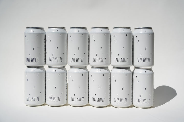 Twelve Love White Can Pack cans by Broc Cellars, arranged in three rows of four, feature minimalistic black "LIVE MINUTE" text with small black marks on a white background, suggesting a California white wine from organically farmed grapes.