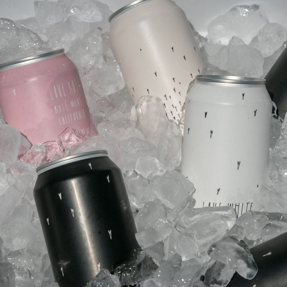 Several Broc Cellars Love Can Variety Pack cans in pink, white, and black—sporting minimal teardrop patterns—chill on ice. These drinkable wine cans are perfect for your next picnic or outdoor get-together.