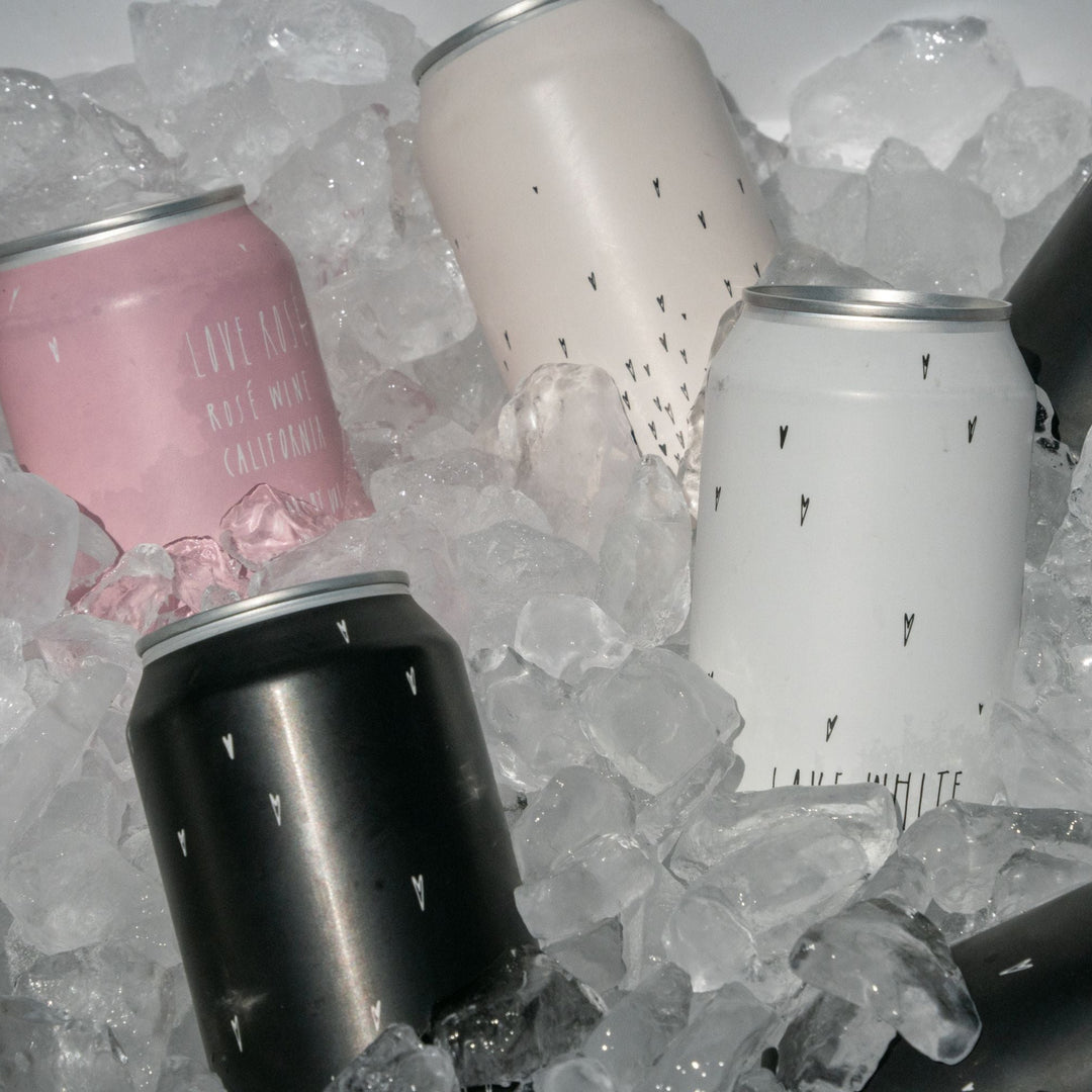 Several Broc Cellars Love Can Variety Pack cans in pink, white, and black—sporting minimal teardrop patterns—chill on ice. These drinkable wine cans are perfect for your next picnic or outdoor get-together.