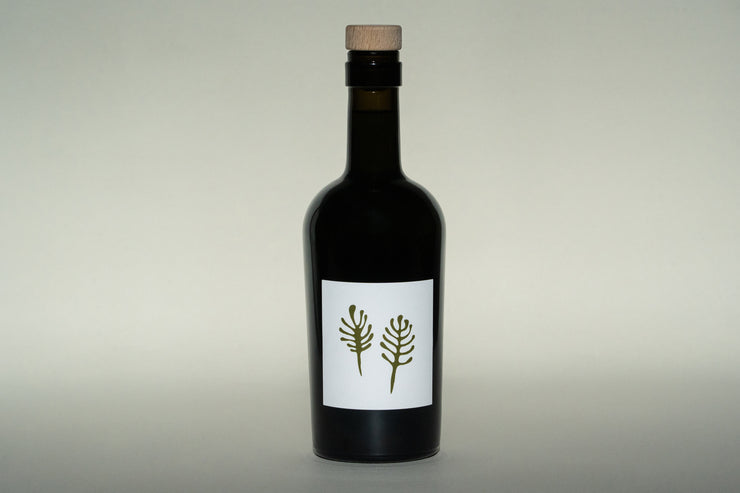 A dark green bottle with a wooden cork cap, exclusive for Club Only members, features a minimalist white label with two fern-like plants. Its the 2024 Olio Nuovo by Broc Cellars, ideal for those joining the club in November 2024.