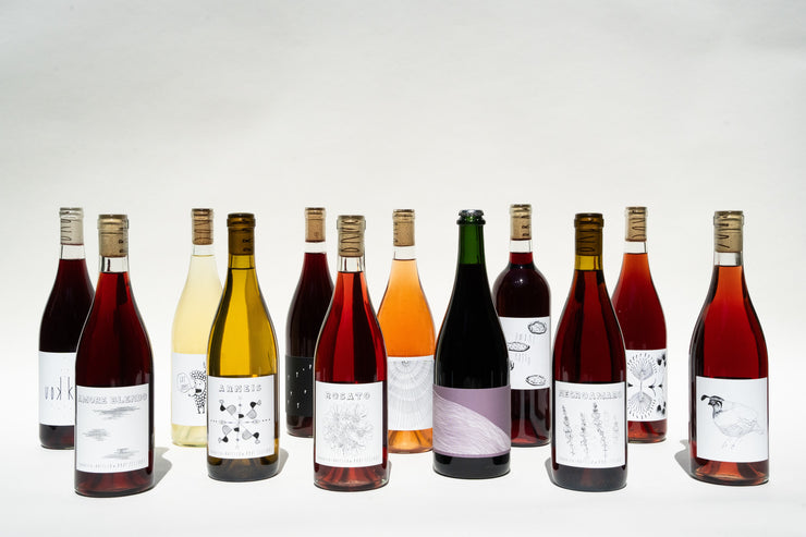 The BROC Collection by Broc Cellars showcases twelve wine bottles in three rows on a light background. Ideal for dinner parties, this assortment ranges from white to red wines, each with unique artistic labels and sealed with natural corks.