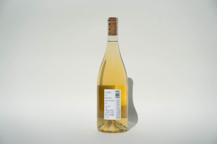 A clear glass bottle of 2024 Got Grapes White wine from Broc Cellars stands against a white background, highlighting its Orange Muscat variety. The label reflects the regions commitment to organic farming. Shadows on the right enhance its elegant silhouette.