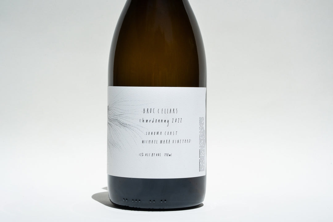 The stylish label of this wine bottle displays Broc Cellars, Sonoma Coast Chardonnay 2022, sourced from the esteemed Michael Mara Vineyard. With a 12% alcohol content, it rests against a neutral white background, highlighting its refined simplicity.