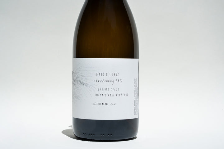 The stylish label of this wine bottle displays Broc Cellars, Sonoma Coast Chardonnay 2022, sourced from the esteemed Michael Mara Vineyard. With a 12% alcohol content, it rests against a neutral white background, highlighting its refined simplicity.