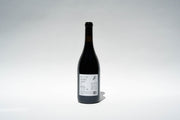 A dark bottle from Broc Cellars, marked 2023 Nero DAvola, stands upright against a plain background. The white label shows text and an illustration, but details arent distinct. A faint shadow is cast on the surface.