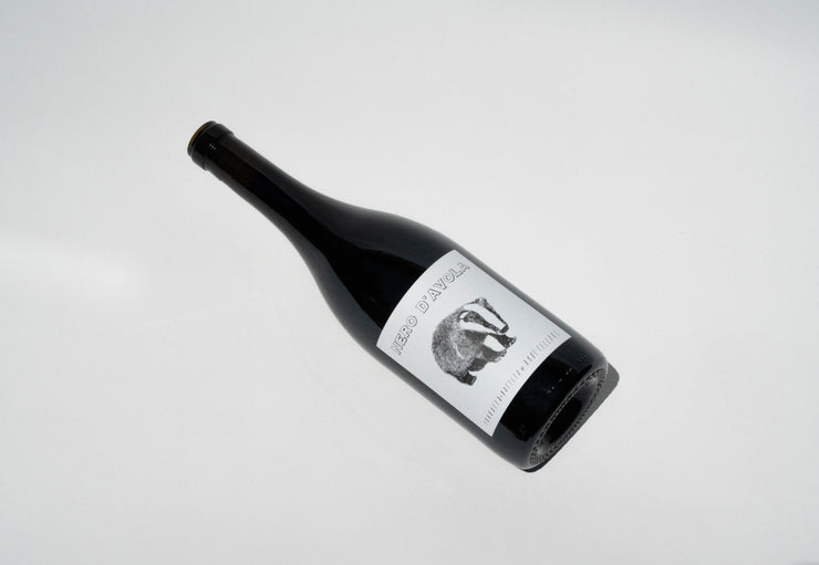 The 2023 Nero DAvola from Broc Cellars features a dark label with a badger illustration, elegantly tilted on a white background. This wine hails from Fox Hill Vineyard in Mendocino, promising curiosity and delight.