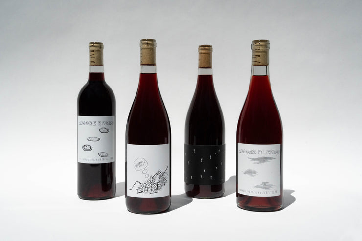 Four bottles of Everyday Reds by Broc Cellars, each with a cork stopper, stand against a white background. Their abstract black and white designs hint at the affordable wine inside. The deep red hue promises a delightful experience for any occasion.