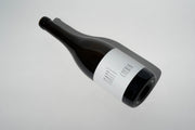 A bottle of organic wine lies on its side against a plain white background. The dark glass features a minimalist label that reads Broc Cellars. Its neck is sealed with a dark cap, casting a subtle shadow, evoking the elegance of 2023 Happī Chenin Blanc.