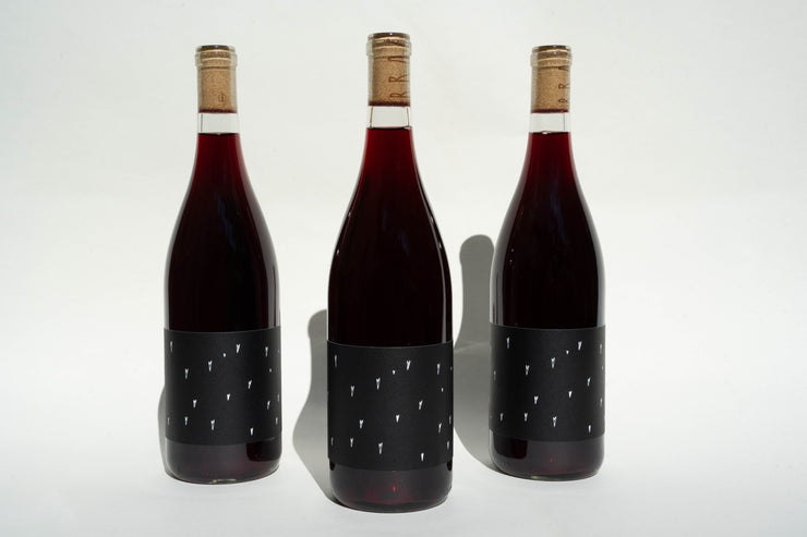 The Love Red Trio from Broc Cellars consists of three 2022 Love Red wine bottles with cork tops and minimalist dark labels with white vertical lines. Elegantly presented, they stand upright in a gift box on a plain white surface.