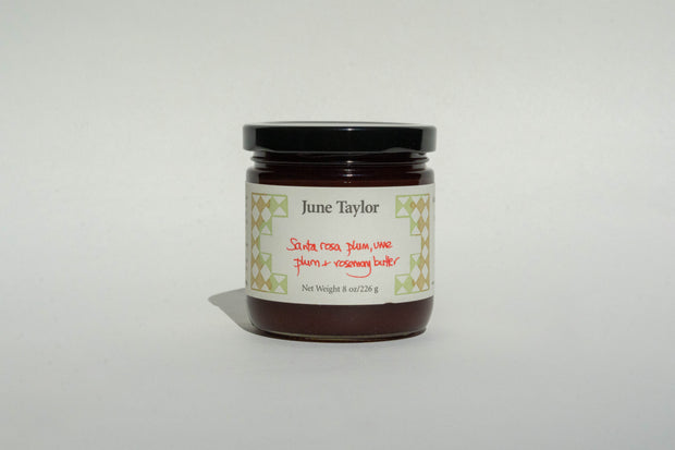 A jar with a black lid labeled Broc Cellars contains an 8 oz (226 g) low-sugar Santa Rosa and Ume plum, rosemary butter by June Taylor. It has a decorative pattern label and is set against a plain white background.