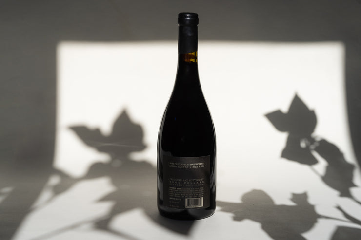 A bottle of 2010 Luna Matta Mourvèdre by Broc Cellars stands against a plain background. Shadows of leaves play around it, highlighting its origins from Paso Robles. The back label provides text details.