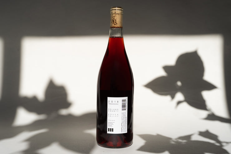 A corked bottle of 2018 TROUSSEAU by Broc Cellars stands against a white background, with leaf shadows casting a serene Russian River Valley ambiance.