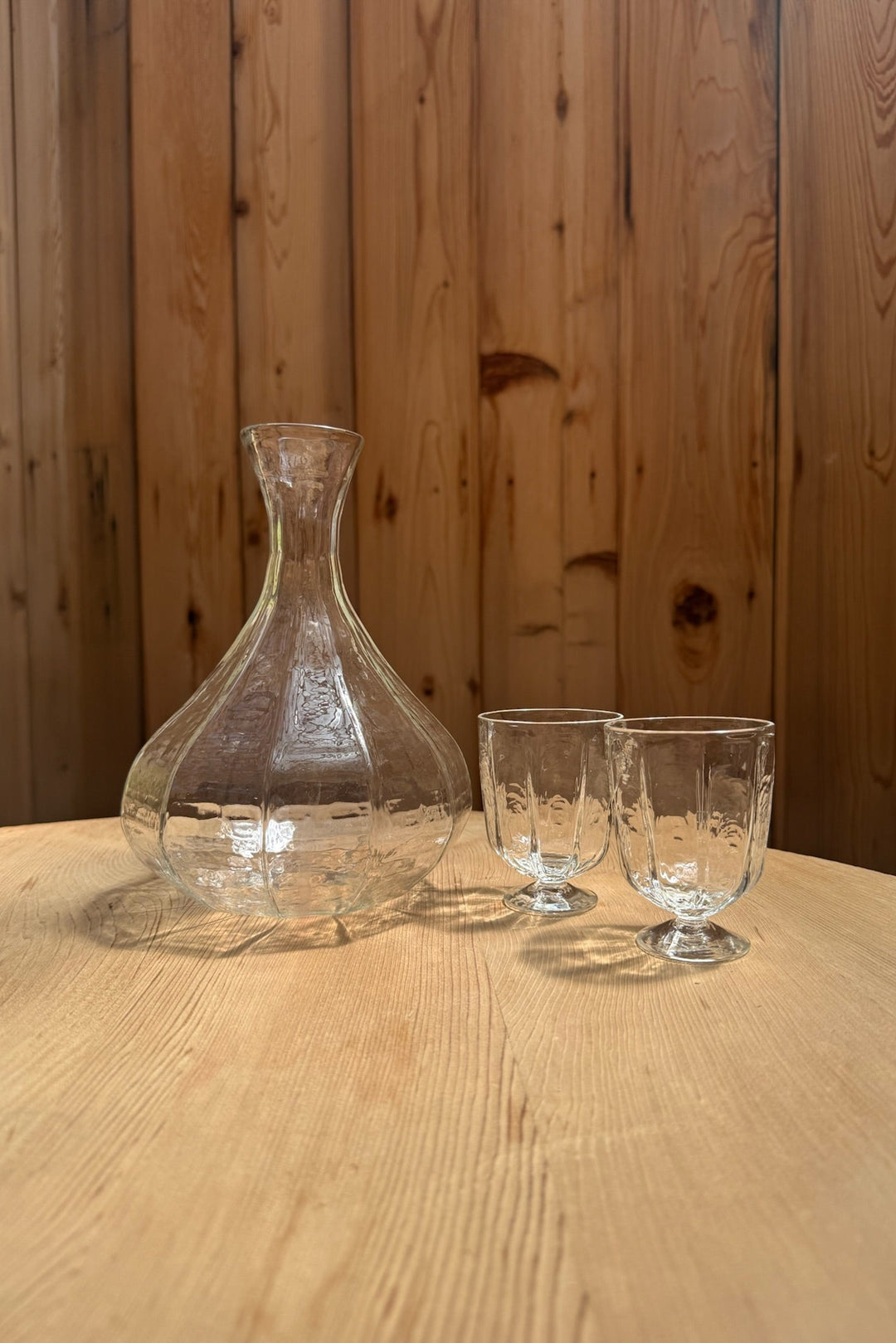 The Broc Cellars Decanter + Glass Set sits on a light wooden table against a wood-paneled wall.