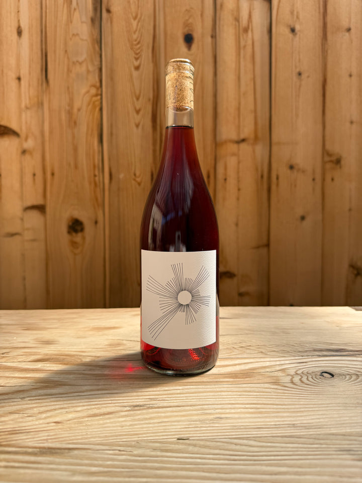A bottle of Broc Cellars 2025 O’Sunshine, sealed with a cork and adorned with a minimalist white label featuring black line art, rests on a light wooden table against a wood-paneled backdrop—perfect for sharing joyful moments or enjoying as part of your favorite Wine Club selection.