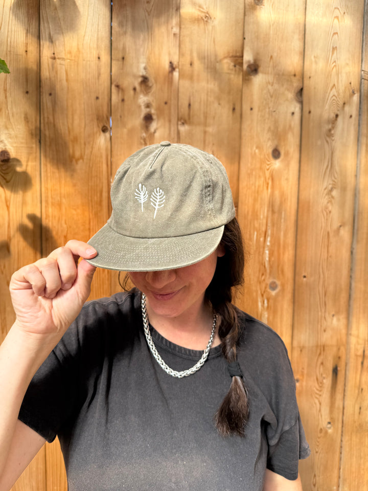 A grey Broc Cellars Fox Hill Field hat in brushed cotton twill, featuring a white line-art illustration of two fern-like plants on the front.