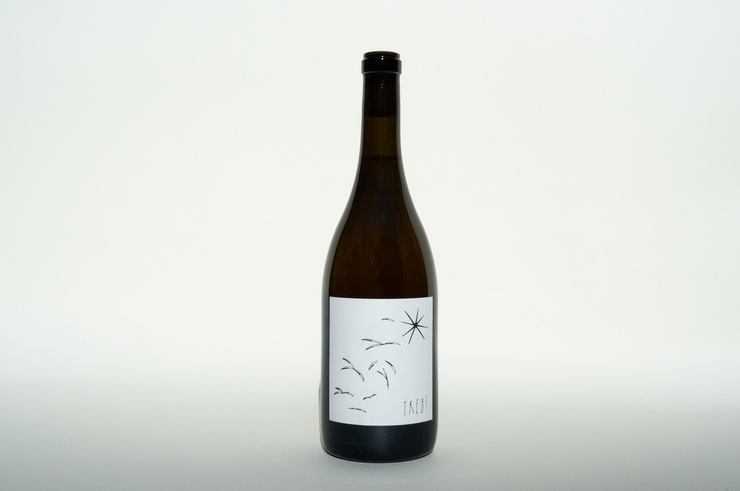 A sleek, dark bottle of 2023 Treb! from Broc Cellars stands against a plain white background, with a minimalistic label showcasing black line drawings of birds and a star. It features an Amore Bianco blend enriched by skin-contact Trebbiano, adding depth to its subtle design.