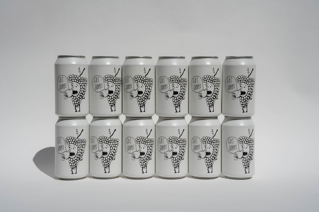 Twelve white cans featuring black line art of a stylized animal with antlers and geometric shapes are arranged in three rows of four. Each can displays “Broc Cellars Got Grapes Red Can Pack,” a chillable red Grenache blend.