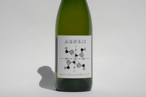 A green bottle of Broc Cellars 2024 Arneis features a white label with ARNEIS at the top and an abstract black geometric design below, reflecting its organic origins. The bottle casts a shadow against a plain, light background.