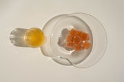 A small glass of Amore Bianco by Broc Cellars sits beside a clear bowl of Yami Yami Pâte de Vin gummies, both casting strong shadows on a white surface.