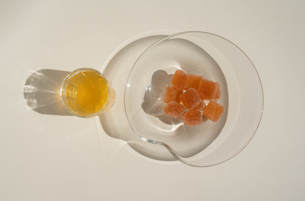 A small glass of Amore Bianco by Broc Cellars sits beside a clear bowl of Yami Yami Pâte de Vin gummies, both casting strong shadows on a white surface.