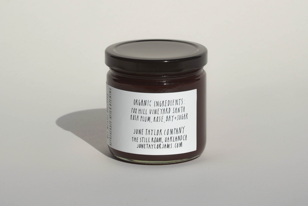 A glass jar of June Taylor x Fox Hill Santa Rosa Plum w/ Bay jam by Broc Cellars features a white label listing organic ingredients and low sugar. Handmade in Oakland, CA, it includes a website for more info.