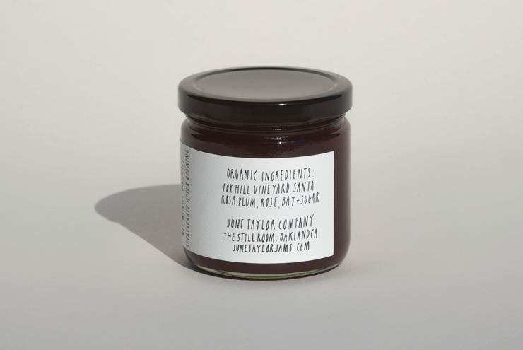 A glass jar of June Taylor x Fox Hill Santa Rosa Plum w/ Bay jam by Broc Cellars features a white label listing organic ingredients and low sugar. Handmade in Oakland, CA, it includes a website for more info.