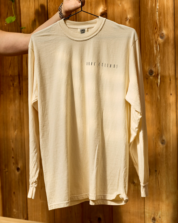 A cream-colored, unisex-fit long-sleeve Berkeley Long Sleeve by Broc Cellars on a hanger, featuring text printed on the upper chest.