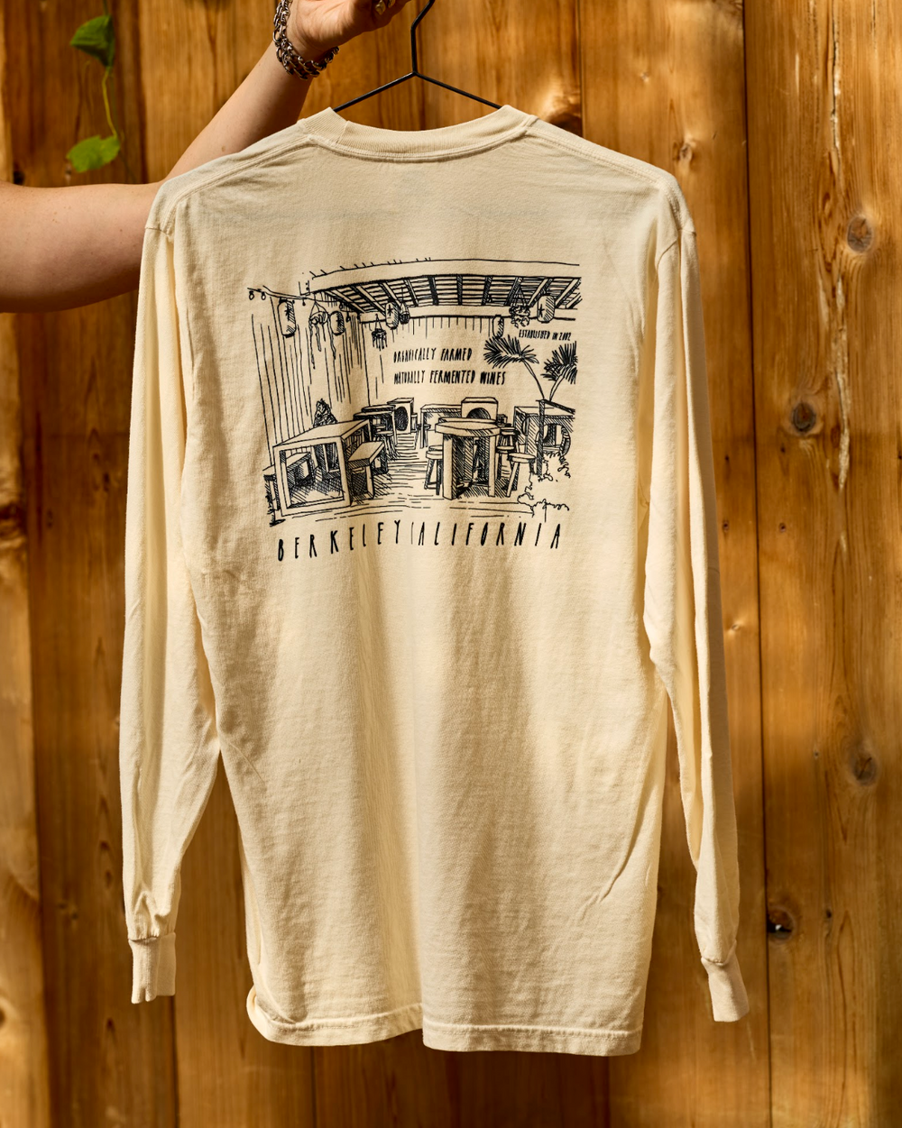 Cream-colored long-sleeve Berkeley Long Sleeve tee featuring a black line-drawing of a restaurant interior and the text Berkeley California on the back.
