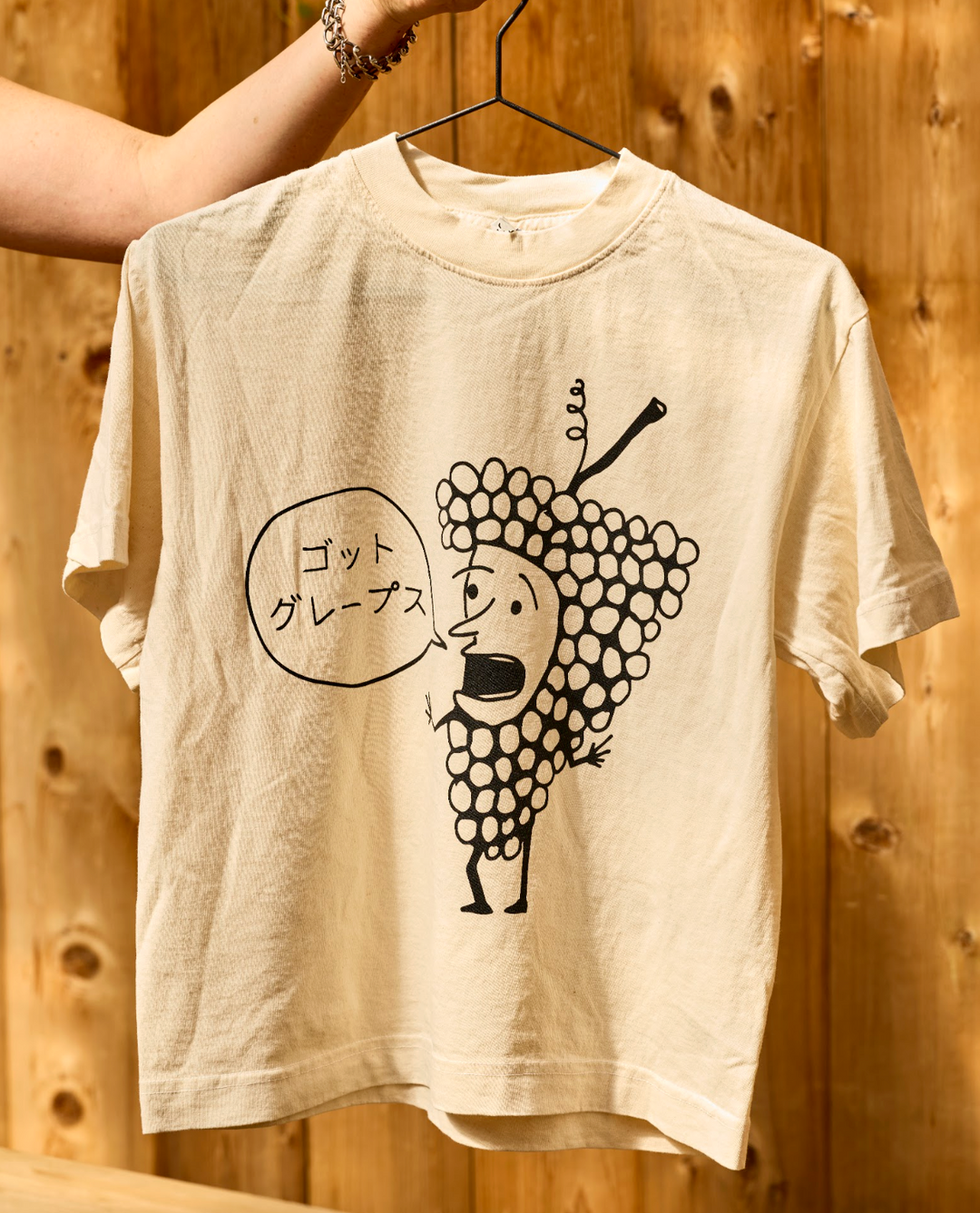 Off-white, unisex oversized Got Grapes T-Shirt featuring a black line drawing of a cartoon grape character with a speech bubble containing Japanese text.