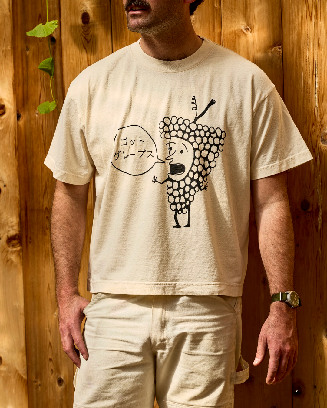 An off-white, unisex oversized Got Grapes T-Shirt featuring a graphic of a cartoon grape character with a speech bubble containing Japanese text.